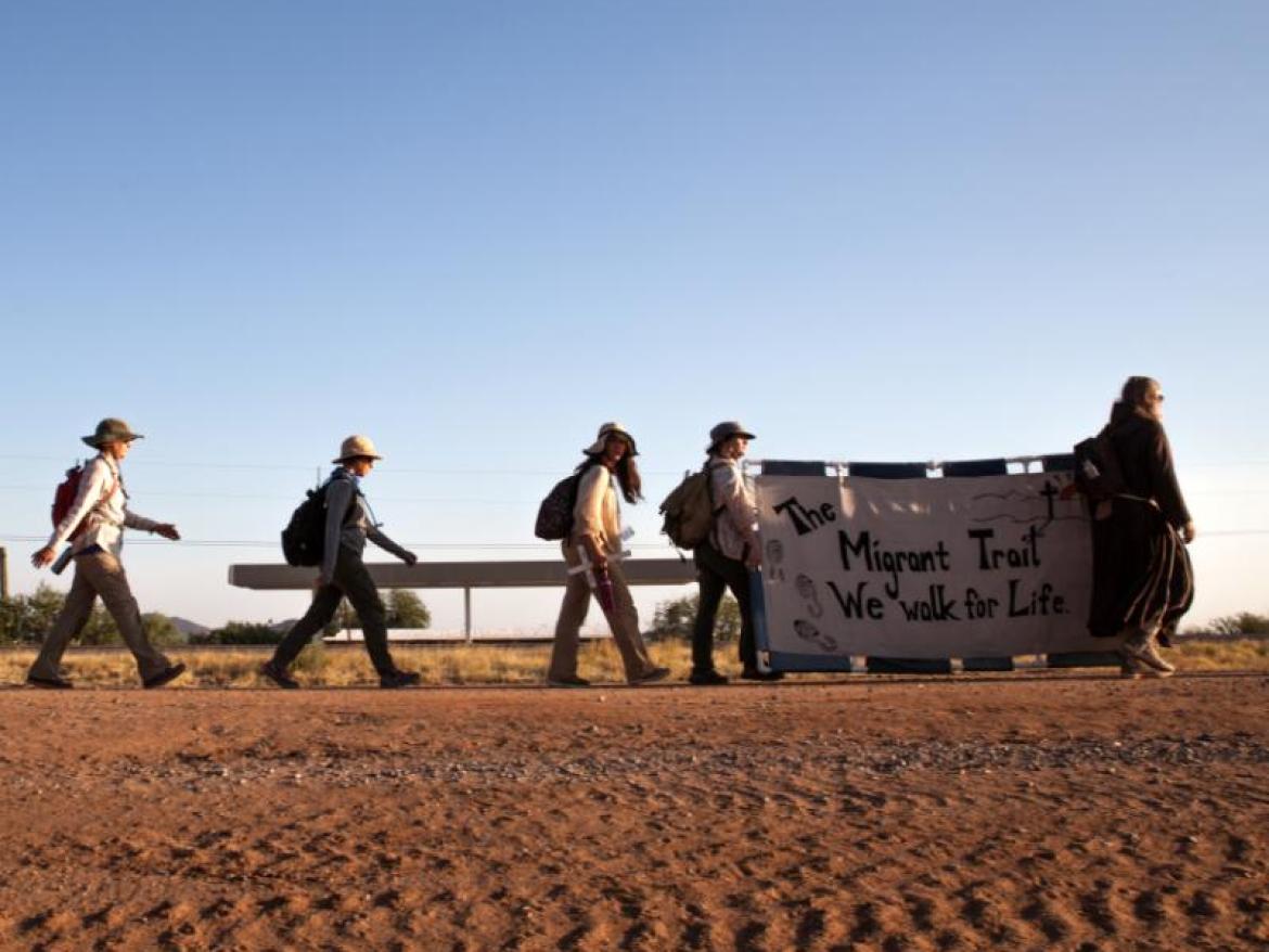 Migrants walking through desert with Banner